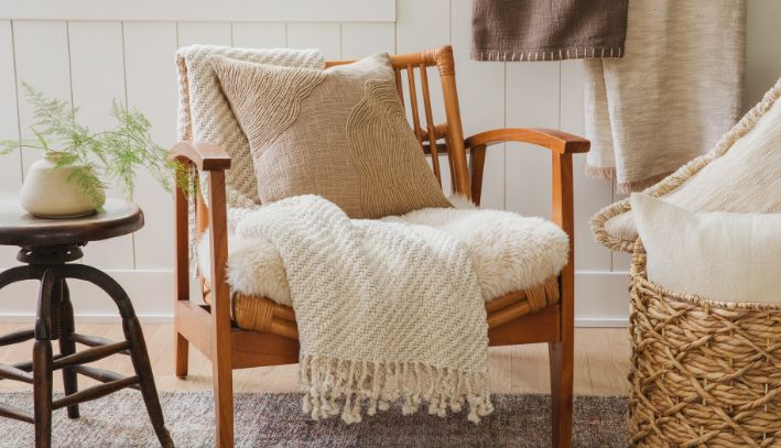 Beige chair with wood arms, draped white blanket, and a small accent pillow