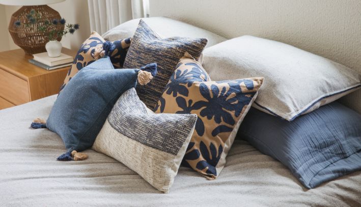 Stacked blue and white pillows with various patterns on a patterned bench