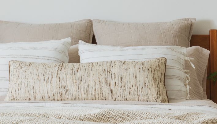 White bedding with textured details and two large white pillows in a softly lit bedroom