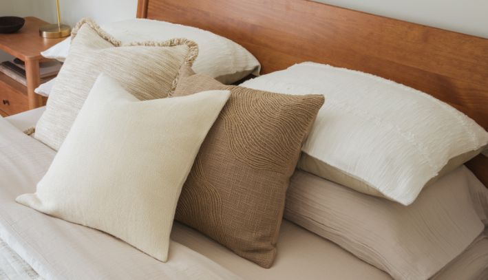 White bed with layered beige and cream pillows and a tan throw blanket