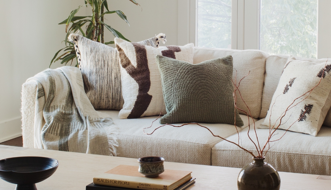 Beige sofa with assorted neutral and green throw pillows, next to a wooden coffee table with a black mug