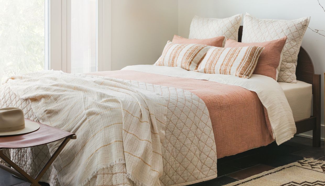 Bed with soft beige bedding, white pillows, and a neutral throw blanket