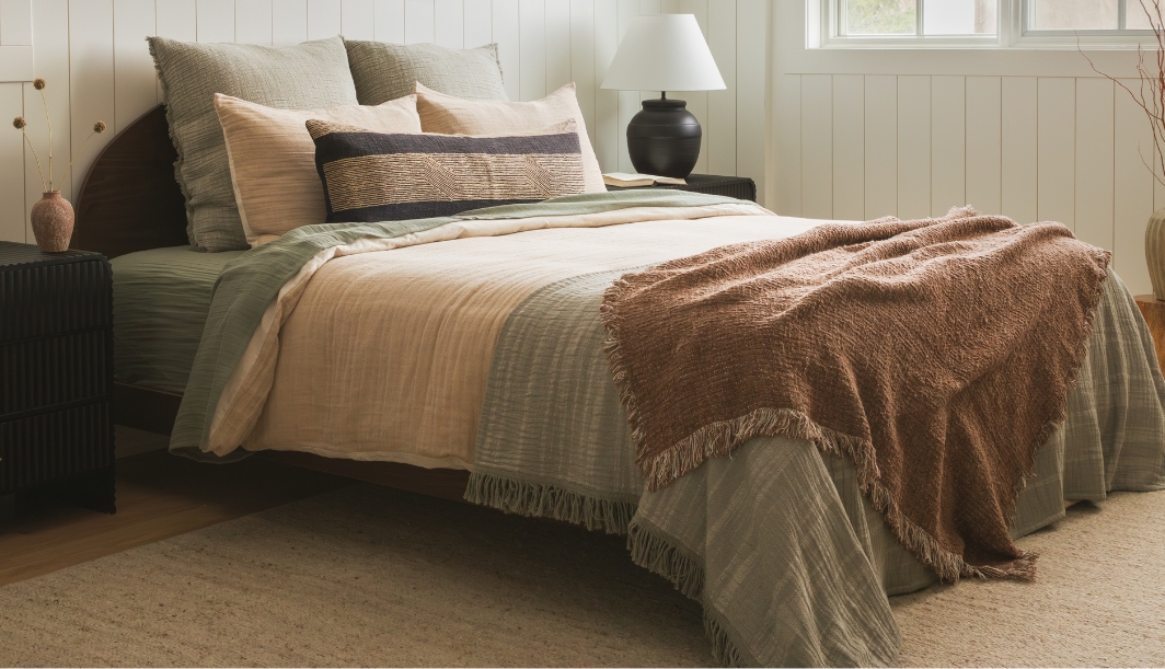 Beige bedding with layered pillows and a rust-colored throw in a modern bedroom