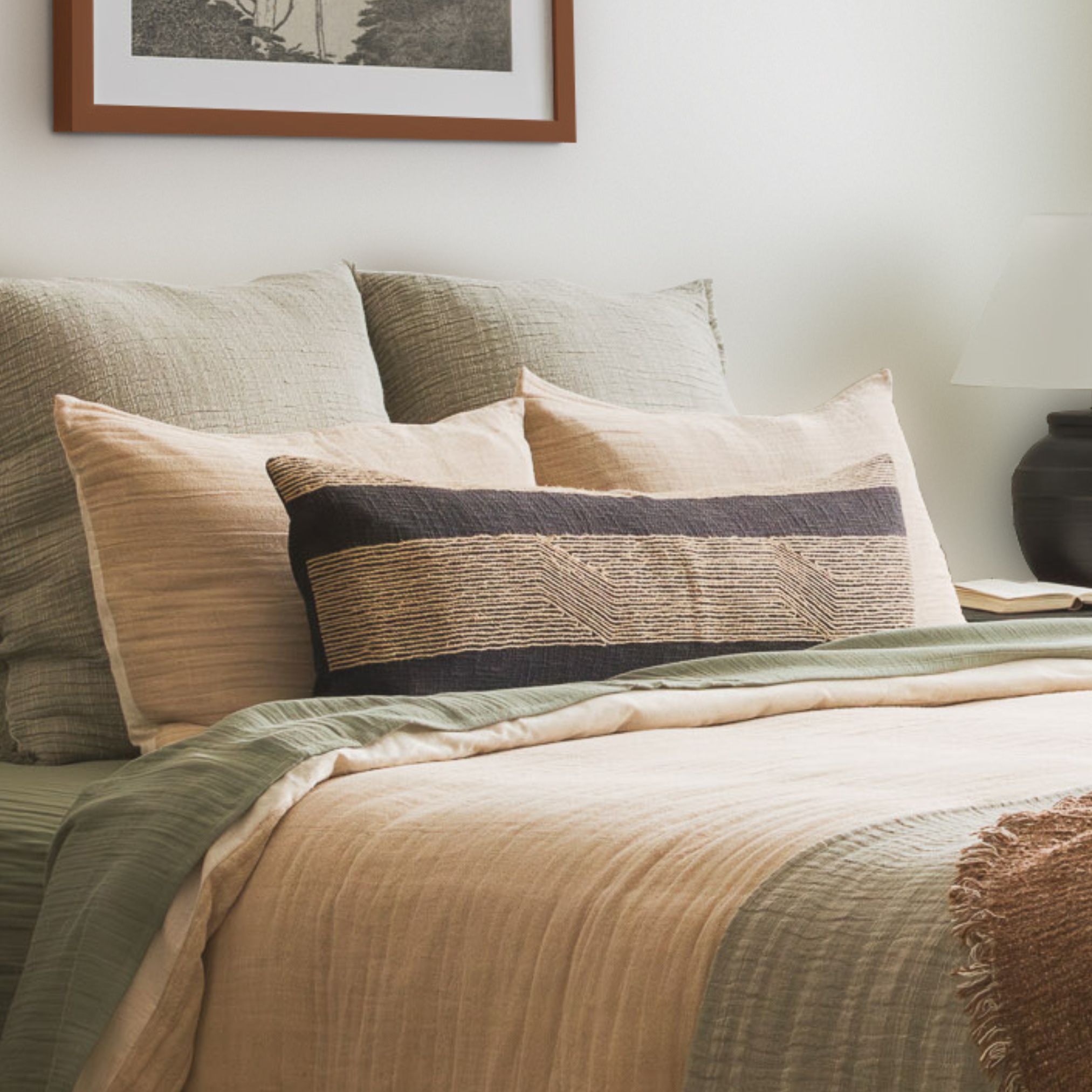 Bedroom scene with sage green bedding, layered pillows, and wooden nightstand