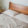 White bed with beige accent blanket and large window in the background