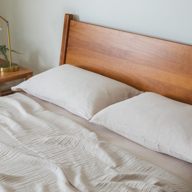 White bed with beige accent blanket and large window in the background