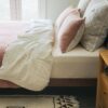 Neutral bed with beige comforter, white pillows, and light wood headboard