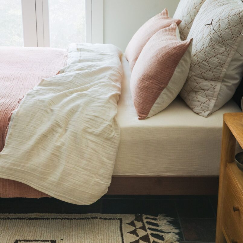Neutral bed with beige comforter, white pillows, and light wood headboard