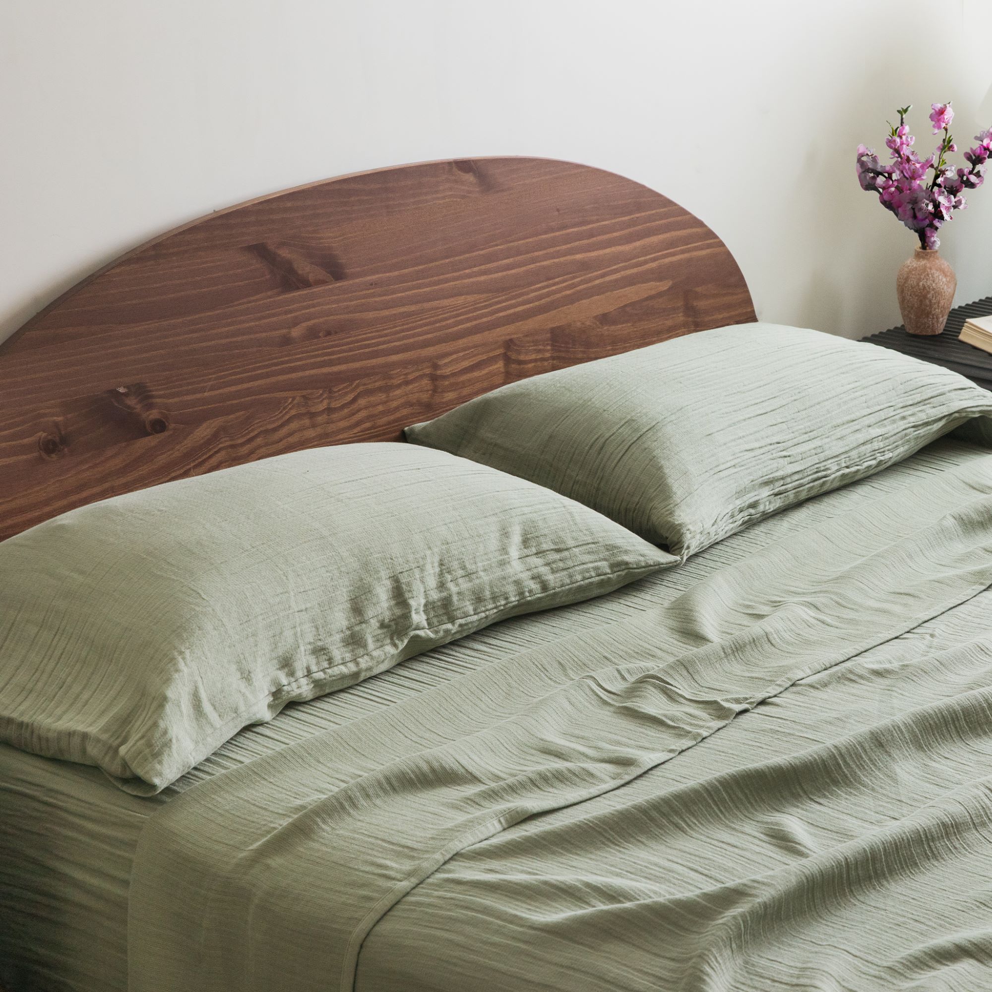 Bed with sage green bedding, rust-colored headboard, and white pillows
