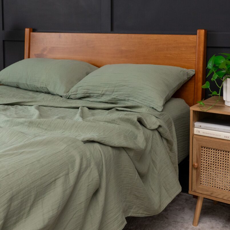 Bed with sage green bedding, matching green pillows, and a light pink background