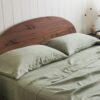 Sage green bedding with layered pillows and a rust-colored headboard