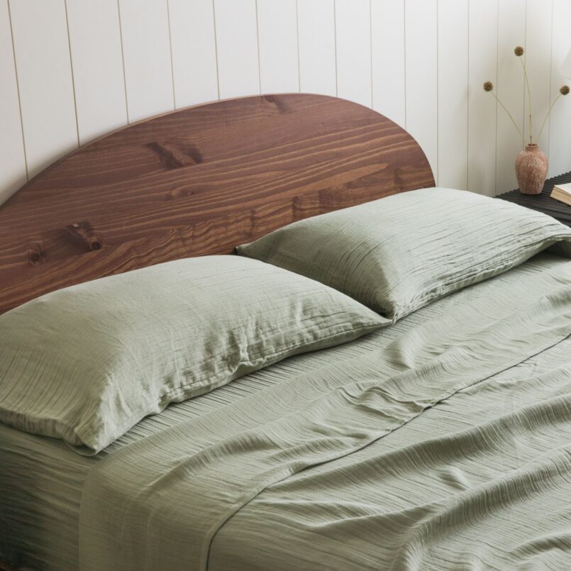 Sage green bedding with layered pillows and a rust-colored headboard