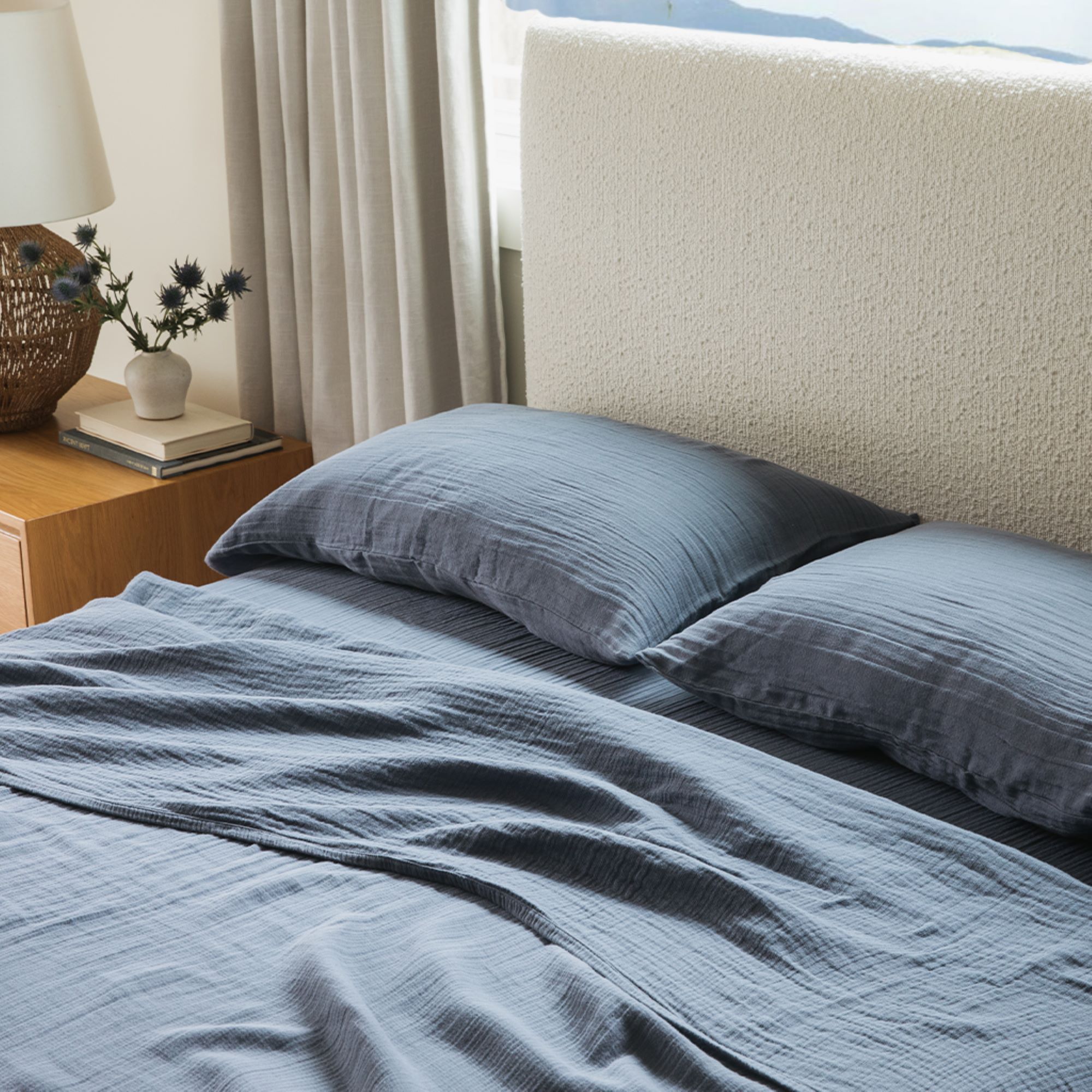 Bed with soft navy bedding and beige accent pillows near a sunlit window