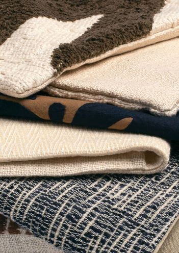 Close-up of folded faux fur and knit blankets stacked on a patterned rug