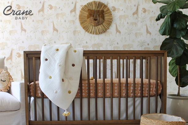 A modern looking nursery , with safari animal themed decor and a brown crib, with a Crane Baby logo in the top left corner