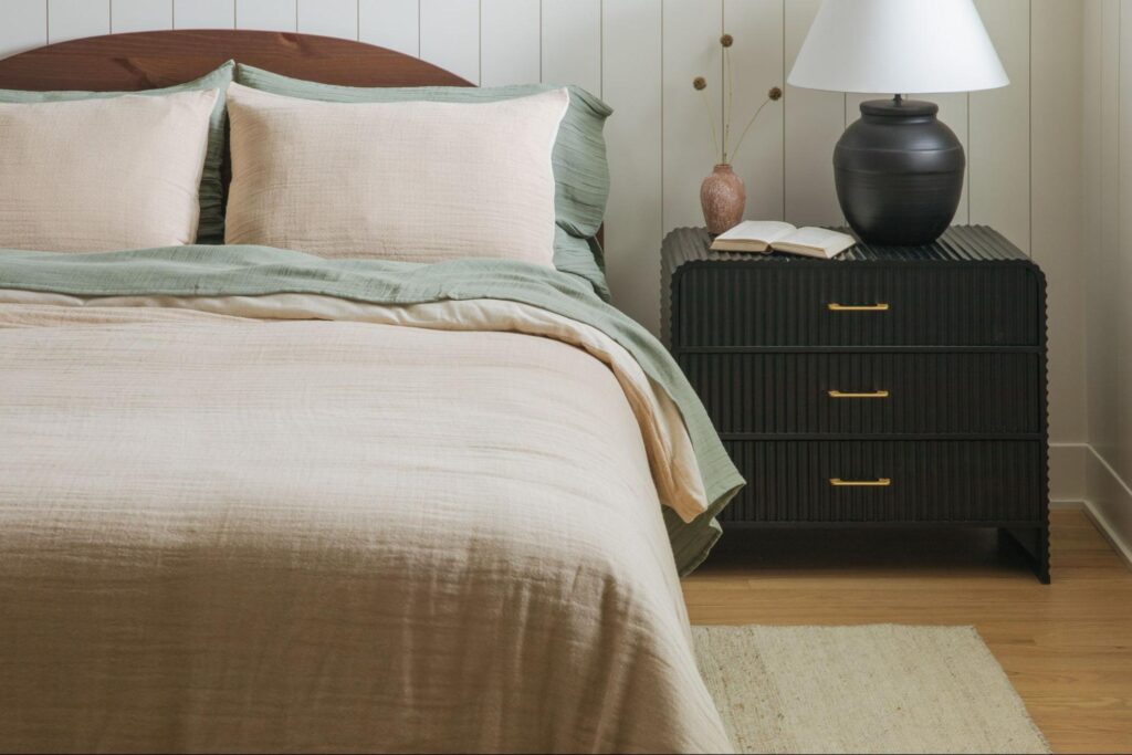 Beige and sage green bed sheets on a bed next to a black nightstand