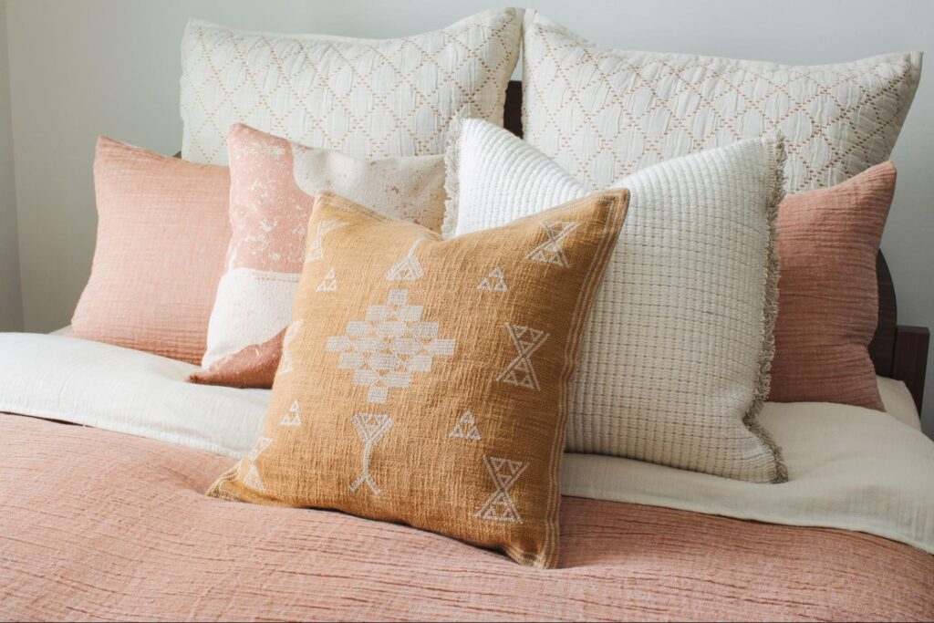 White, rust and orange throw pillows layered on a bed 