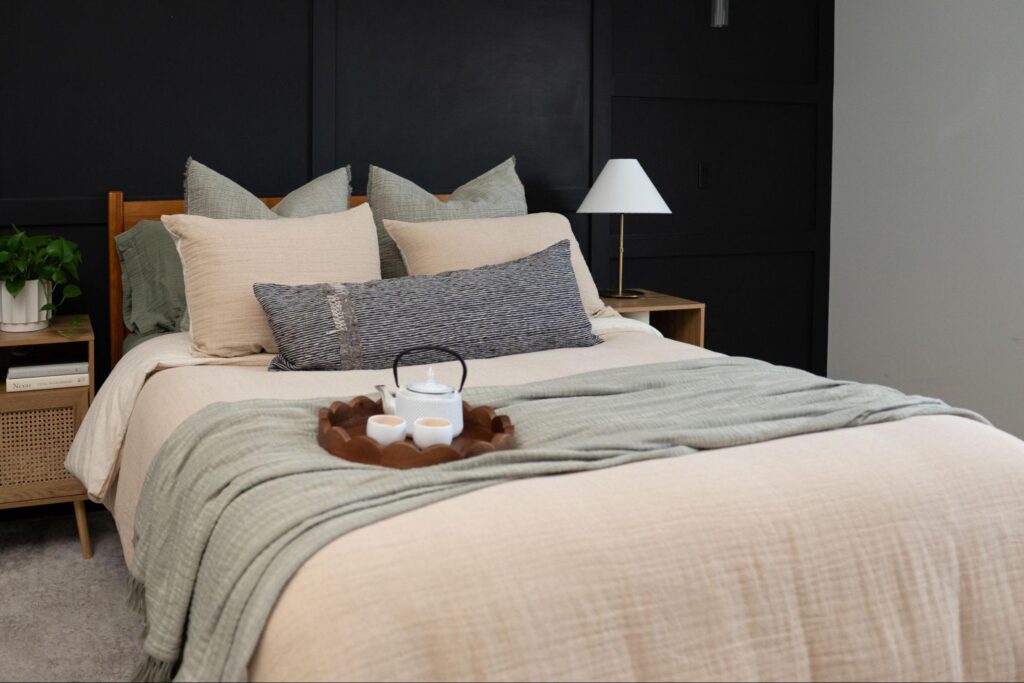 Bed with a tea set on a tray over sage and cream bedding